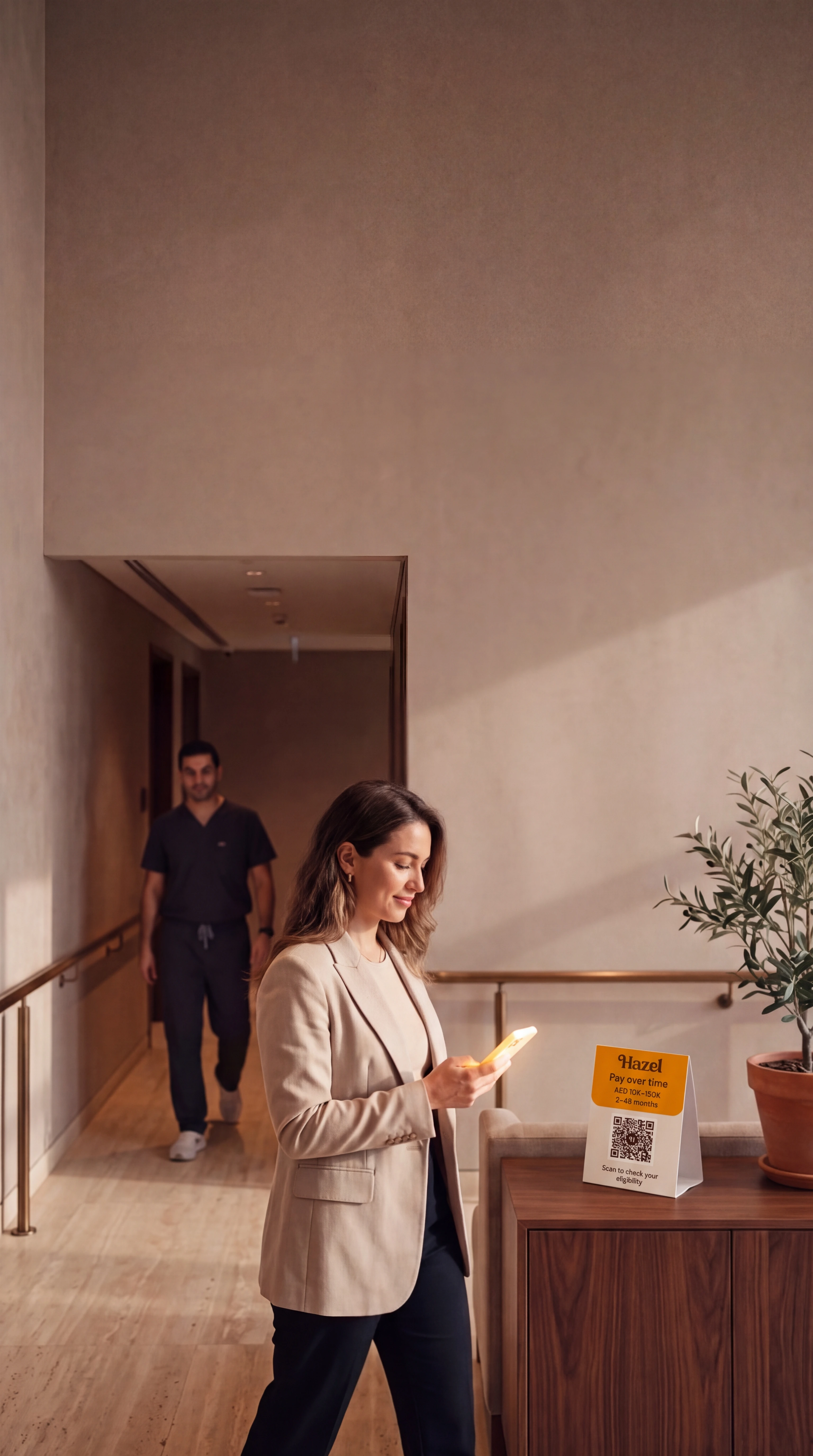 A patient checks a phone in a calm clinic corridor, with a Hazel card on the console alongside.
